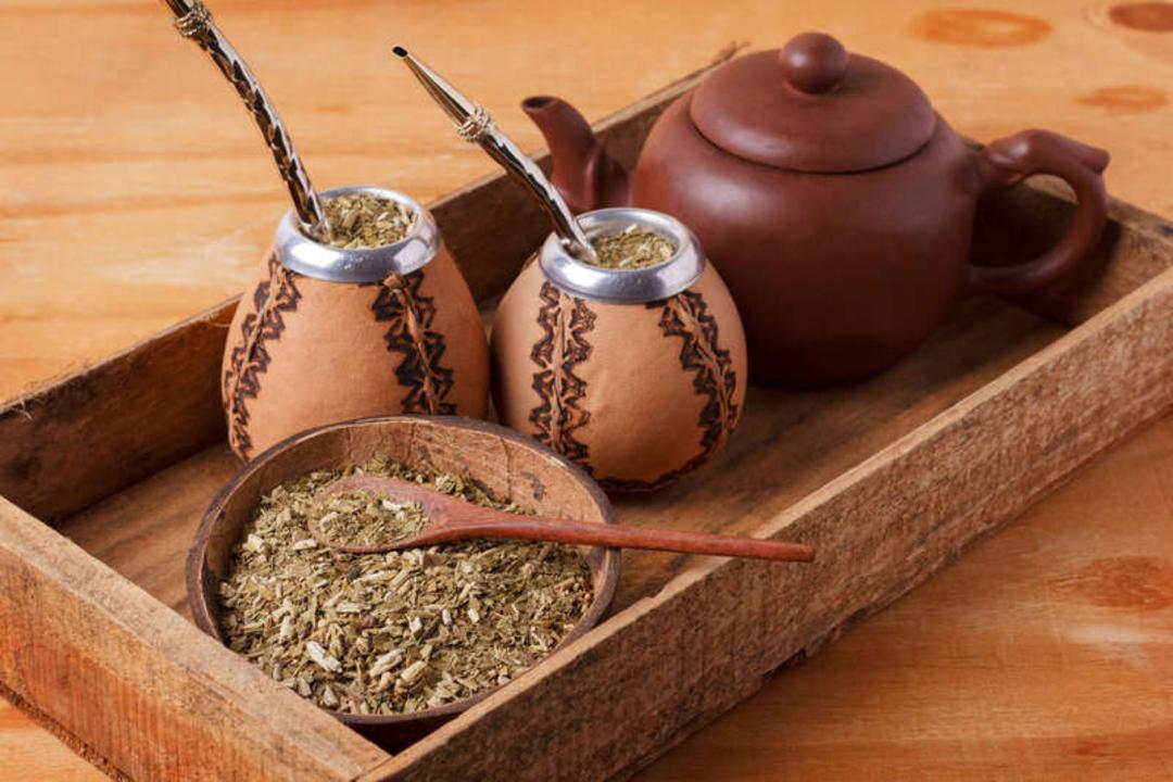 فنجان‌های چای ماته (Mate) همراه با قوری سفالی و برگ‌های خشک در یک سینی چوبی
