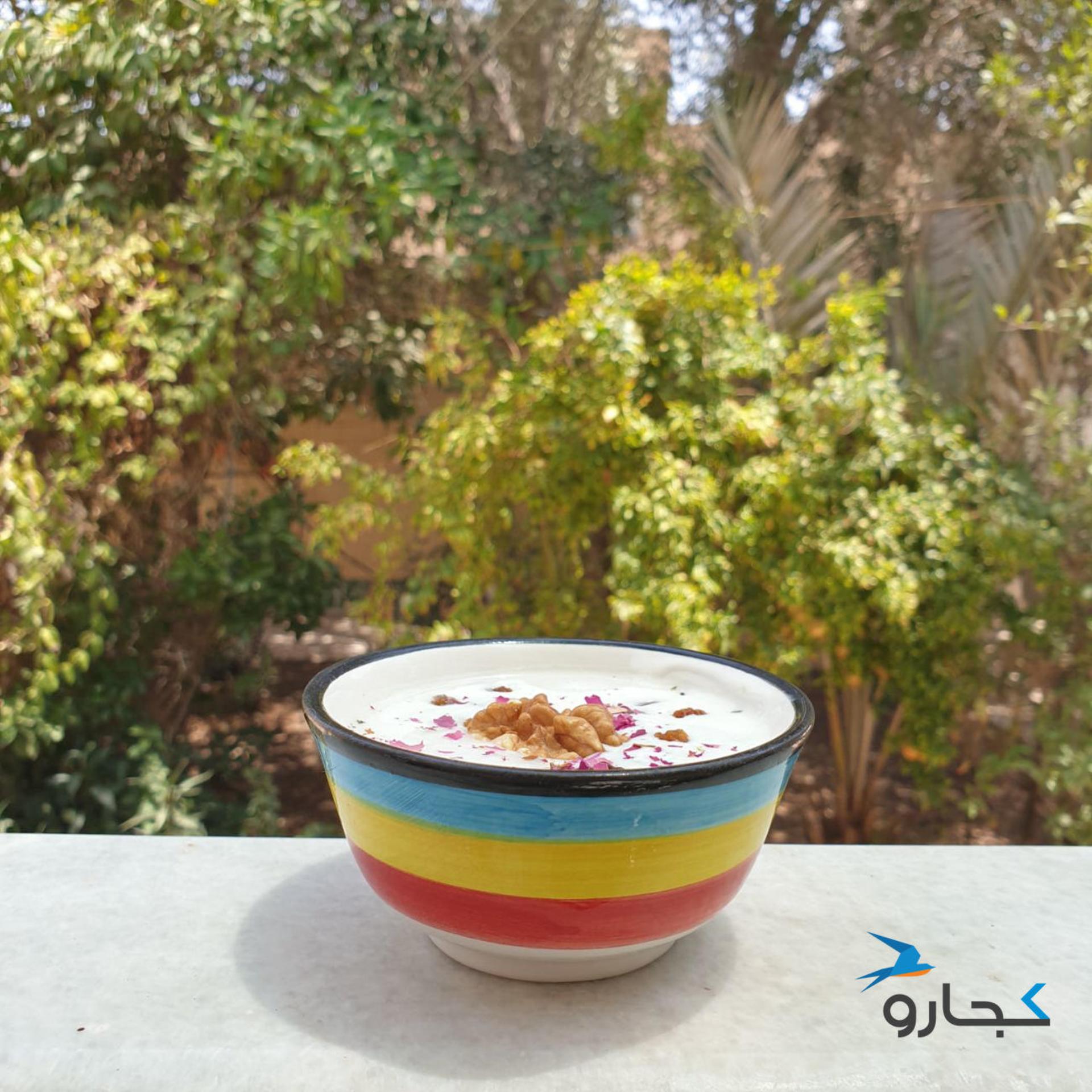کاسه رنگارنگ آب دوغ خیار روی نرده حیاط با پس زمینه درختان