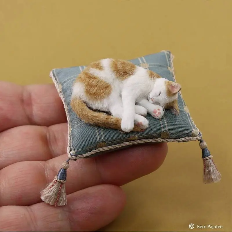 مجسمه بسیار واقع‌گرایانه گربه (Cat) در حال خواب روی یک بالش کوچک آبی