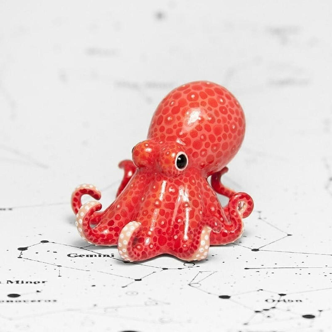 مجسمه مینیاتوری اختاپوس (Octopus) قرمز رنگ با بافت نقطه‌دار روی نقشه نجومی