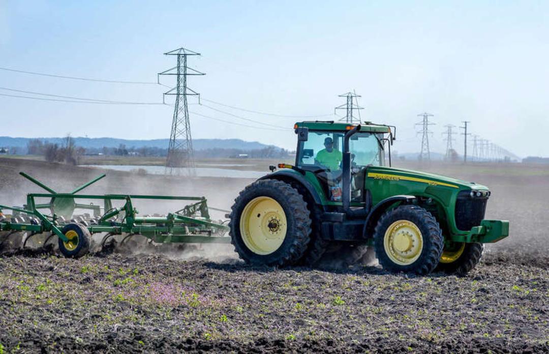 تراکتور (John Deere) در حال شخم زدن زمین کشاورزی در یک مزرعه بزرگ