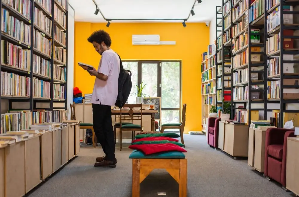 مردی در حال مطالعه کتاب در میان قفسه‌های بلند کتاب‌فروشی دماوند