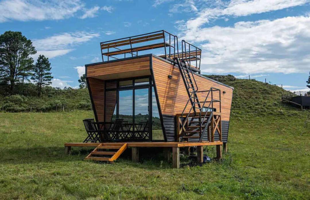 خانه مینیاتوری (Tiny House) با نمای چوبی و پنجره‌های بزرگ در طبیعت