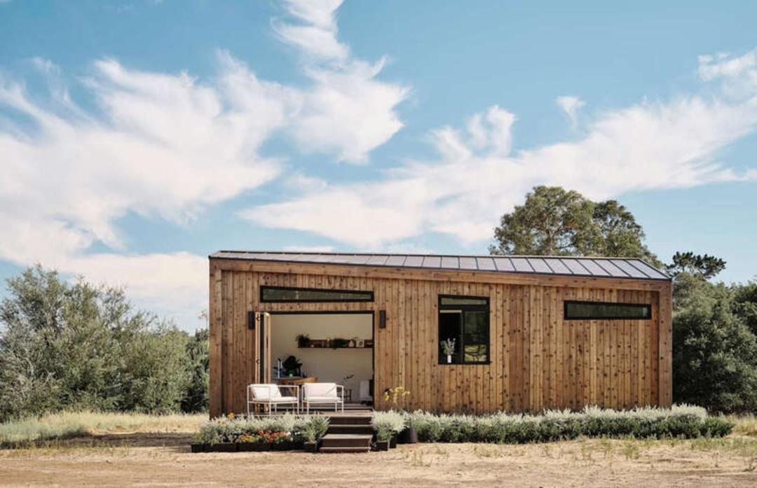 خانه مینیاتوری (Tiny House) با نمای چوبی و پنجره‌های بزرگ در طبیعت