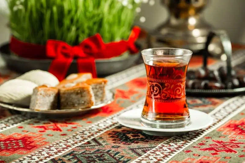 یک استکان چای کمر باریک و شیرینی باقلوا با سبزه نوروز