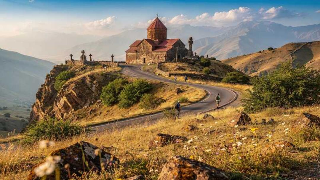 کلیسای قدیمی با سقف قرمز در میان کوه‌های مرتفع و جاده کوهستانی