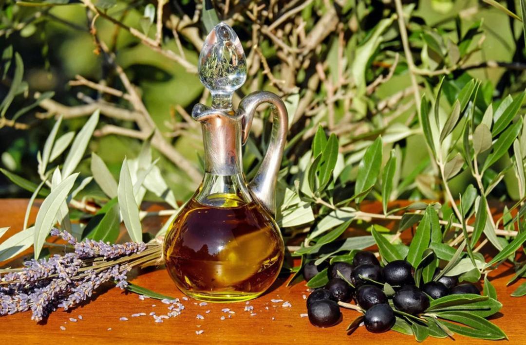 روغن زیتون در ظرف شیشه‌ای کنار زیتون‌های سیاه و شاخه‌های زیتون