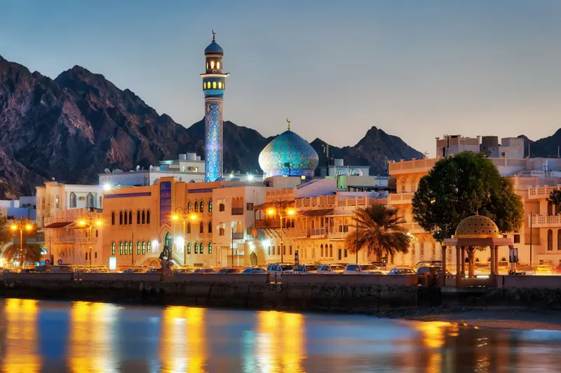 شهر مسقط عمان در غروب با مناره مسجد، گنبد سبز و کوه‌های پس‌زمینه