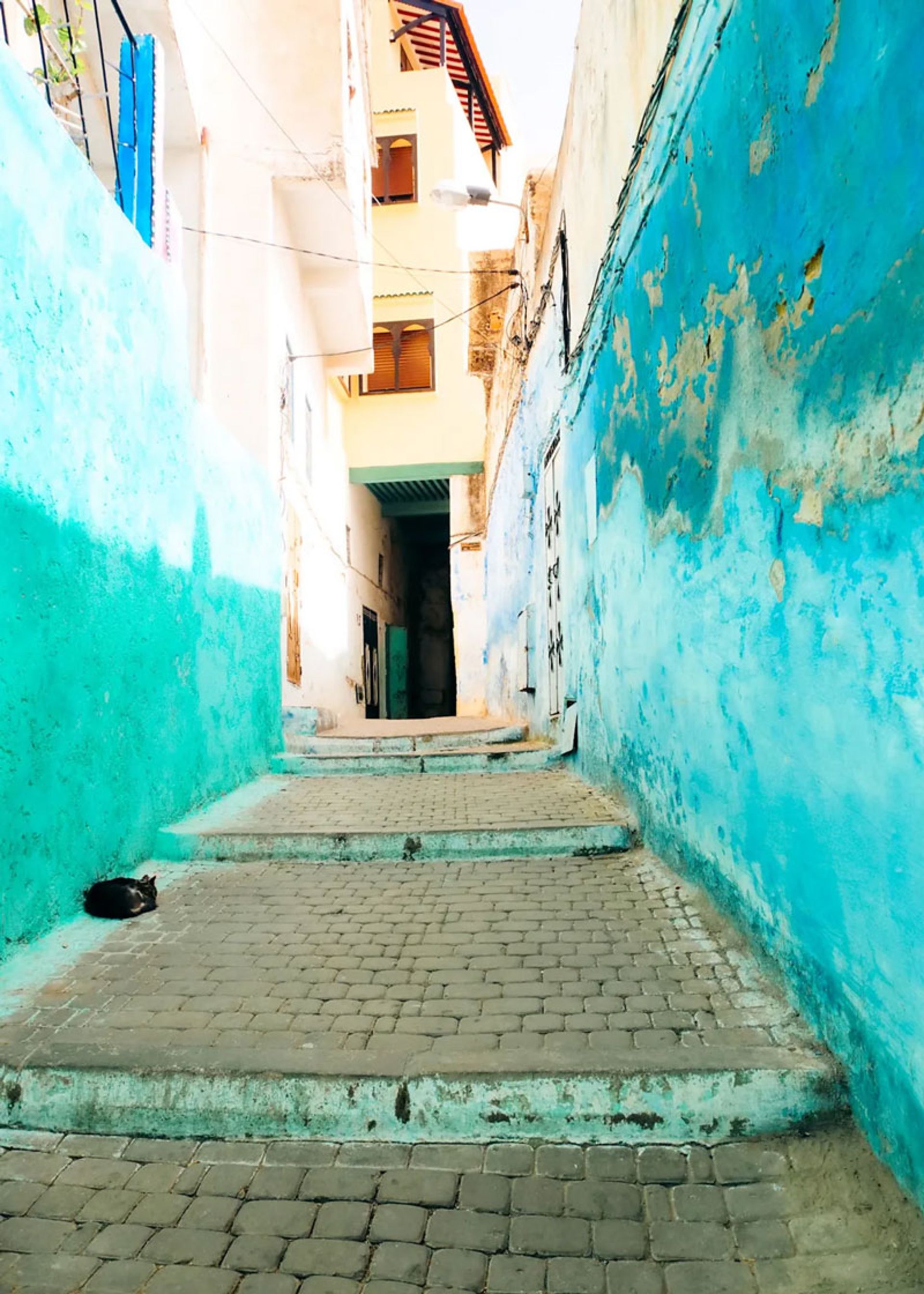 کوچه‌ی باریک و شیب‌دار با دیوارهای فیروزه‌ای و کف سنگی در مولای ادریس