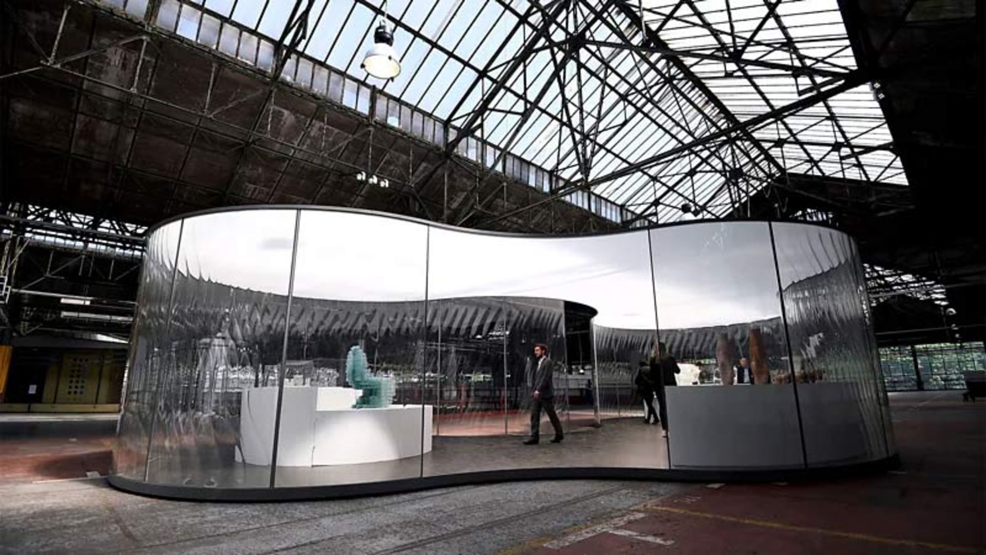 فضای داخلی یک سوله صنعتی بزرگ با سازه فلزی و سقف شیشه‌ای که یک گالری مدرن و منحنی