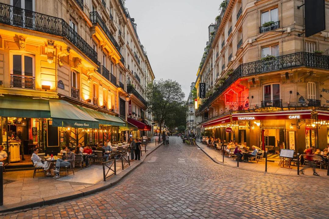 کوچه‌های سنگ‌فرش شده پاریس (Paris) با کافه‌های روشن در دو طرف خیابان