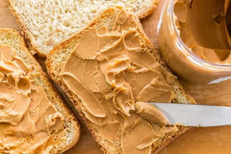 نان تست پوشیده شده با کره بادام زمینی (Peanut Butter) روی تخته چوبی