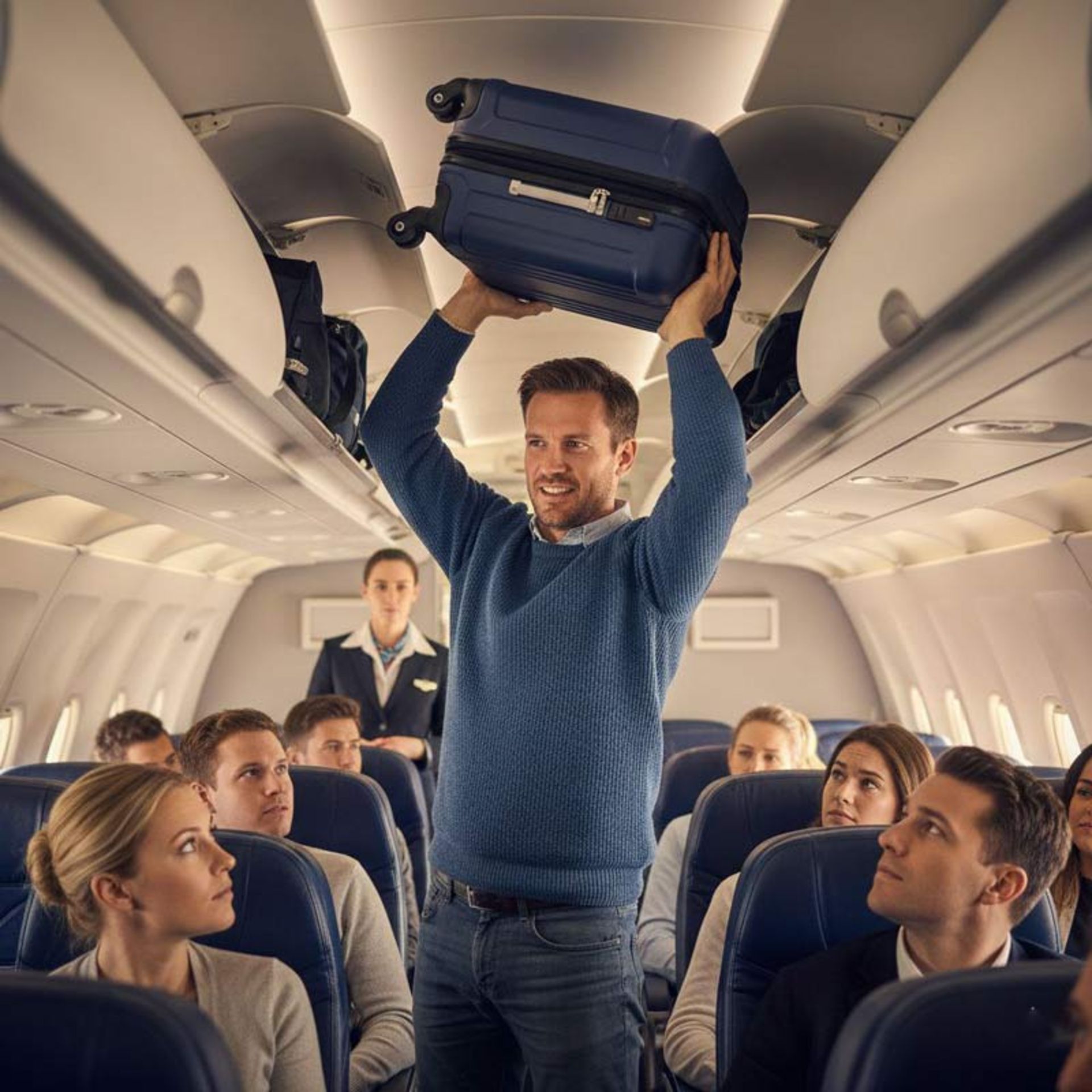 مسافری با پلیور آبی که چمدان سنگین خود را با هر دو دست بالای سر برده