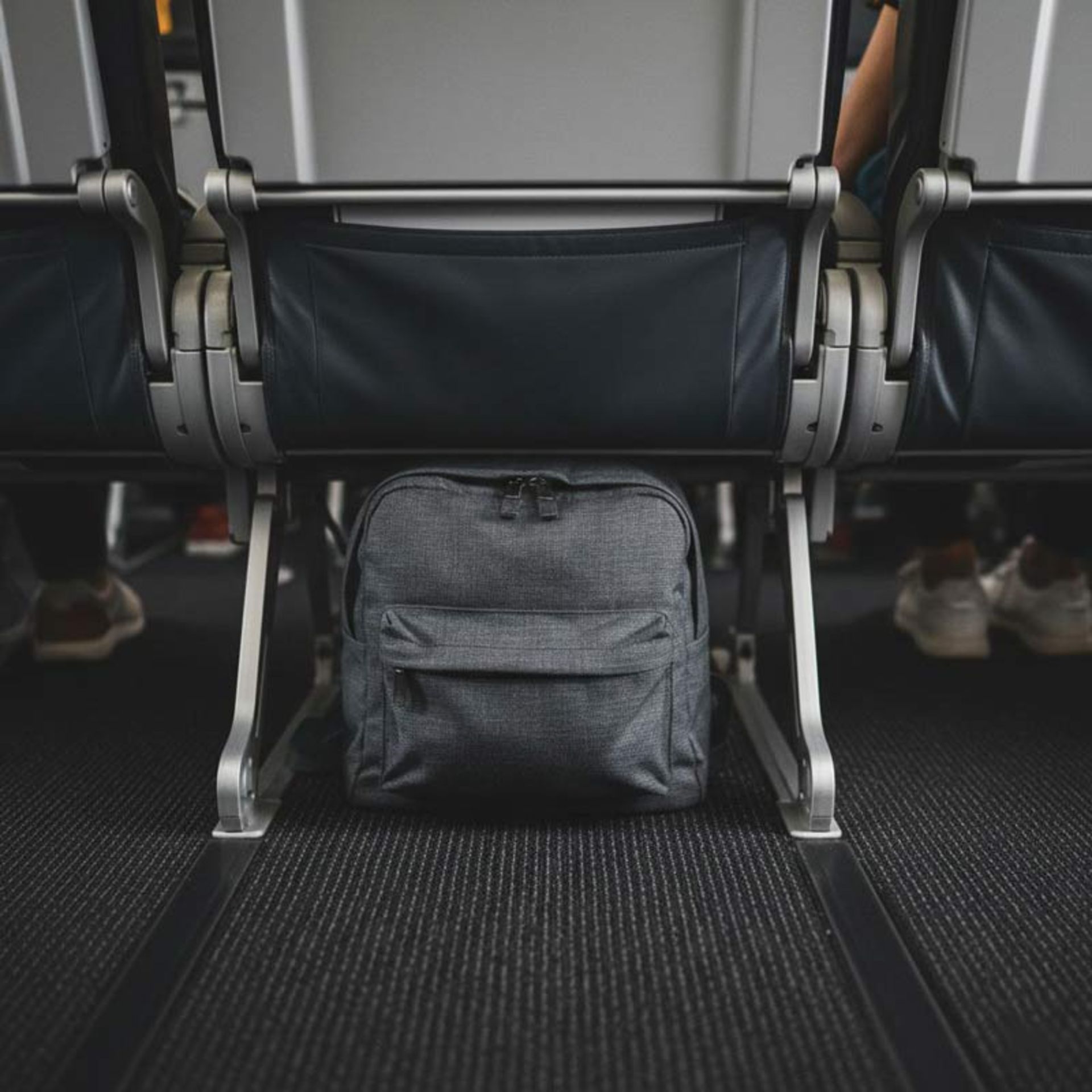 نمای نزدیک از یک کوله‌پشتی خاکستری تیره در فضای زیر صندلی جلویی هواپیما