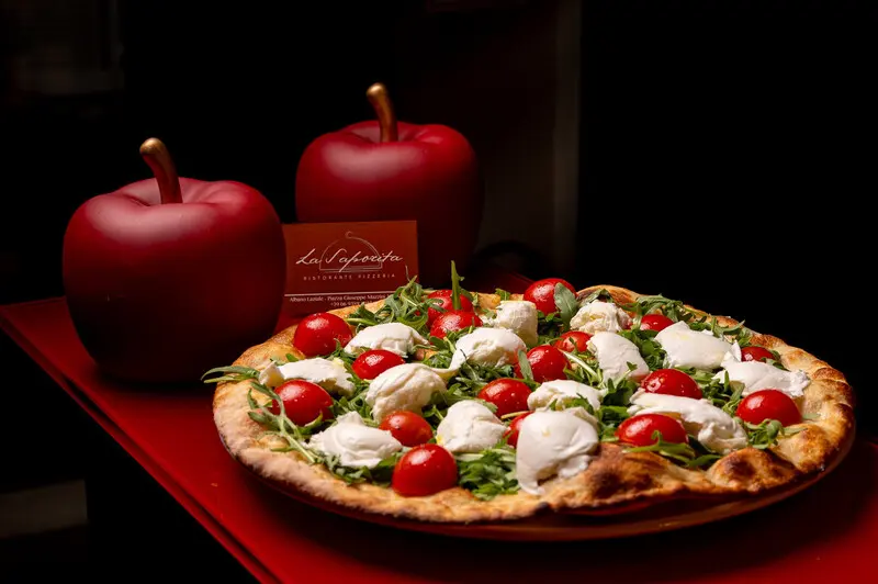پیتزای تازه با پنیر موتزارلا (Mozzarella) و گوجه‌فرنگی روی میز قرمز