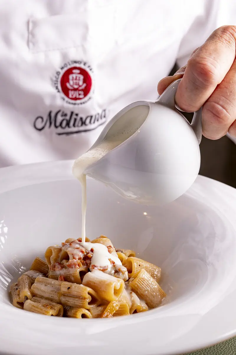 پاستای ریگاتونی (Rigatoni) در بشقاب سفید که سس سفید روی آن ریخته می‌شود
