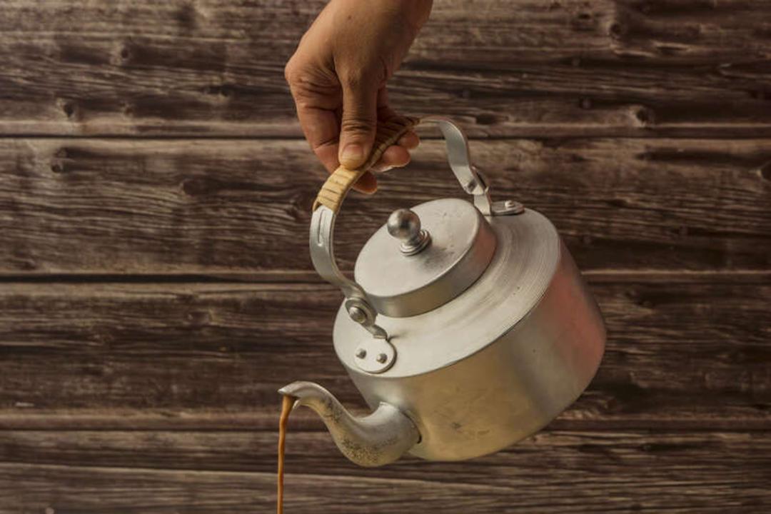 چای در حال ریختن از یک قوری فلزی قدیمی روی پس‌زمینه چوبی
