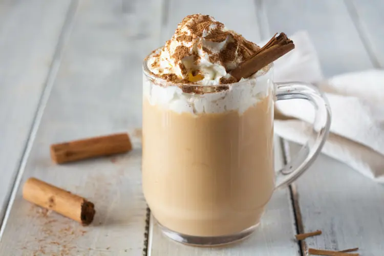 پامکین اسپایس لاته (Pumpkin Spice Latte) با خامه و دارچین در لیوان شیشه‌ای