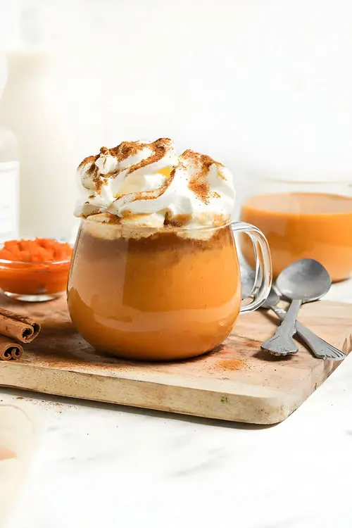 پامکین اسپایس لاته (Pumpkin Spice Latte) با خامه و پودر دارچین در لیوان شیشه‌ای