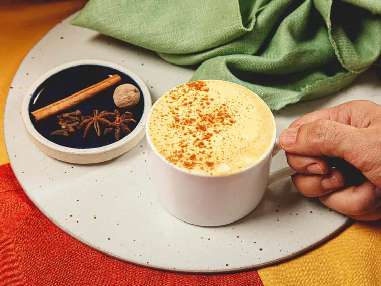 پامکین اسپایس لاته (Pumpkin Spice Latte) در فنجان سفید همراه با ادویه‌های پاییزی