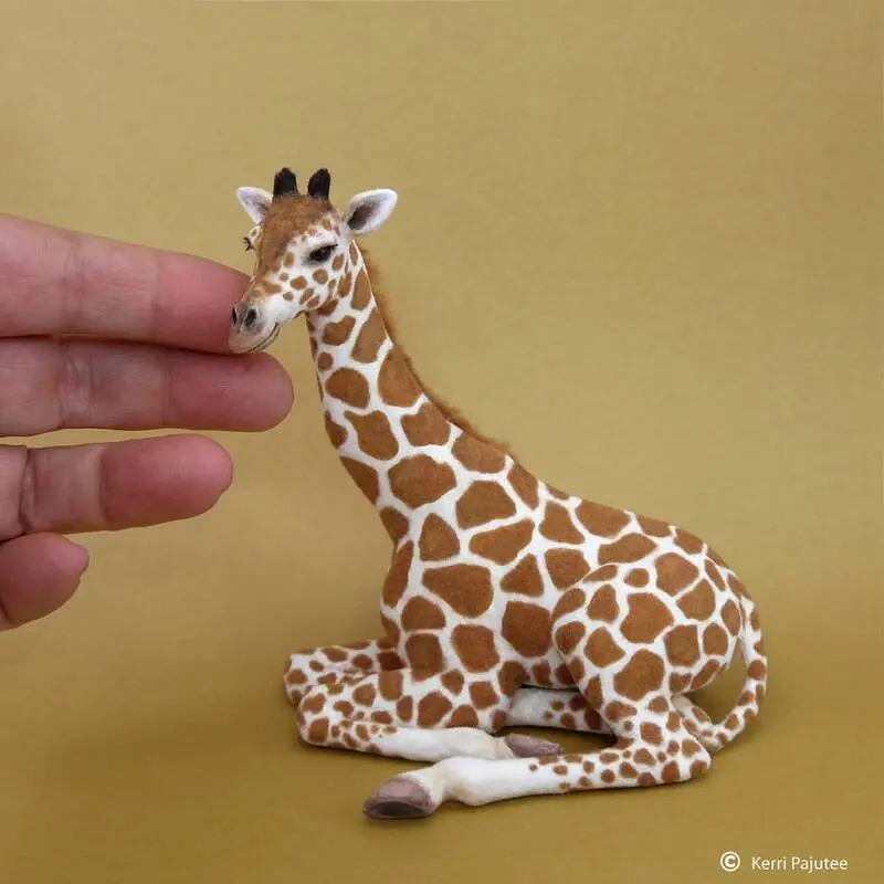 مجسمه زرافه (Giraffe) با طرح خال‌خالی که در دستان یک فرد قرار دارد