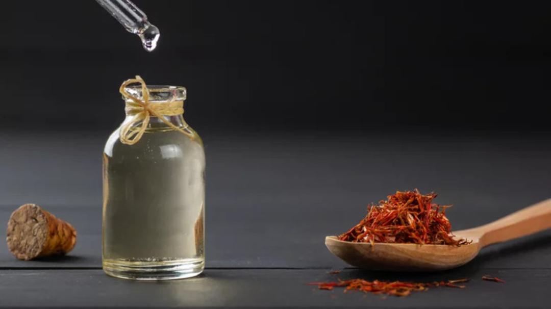 روغن زعفران در یک ظرف شیشه‌ای کوچک در کنار گلبرگ‌های خشک زعفران