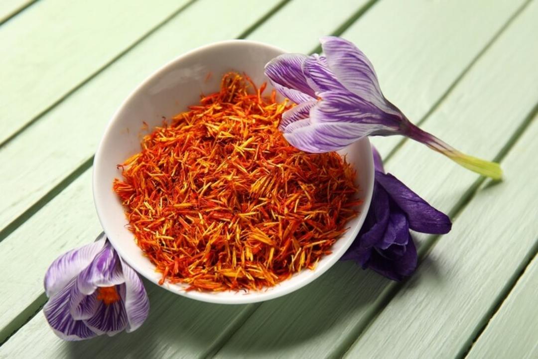 زعفران (Saffron) در یک ظرف سفید در کنار گل‌های بنفش کروکوس