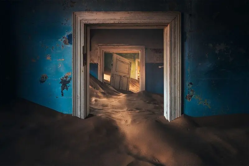 شن‌های روان در میان درگاه‌های چوبی خانه‌های متروکه کولمانسکوپ (Kolmanskop)