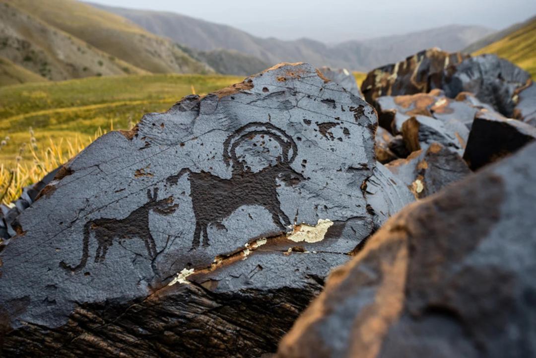 سنگ‌نگاره‌های باستانی (Petroglyphs) حک شده روی صخره‌های تیره در کوهستان