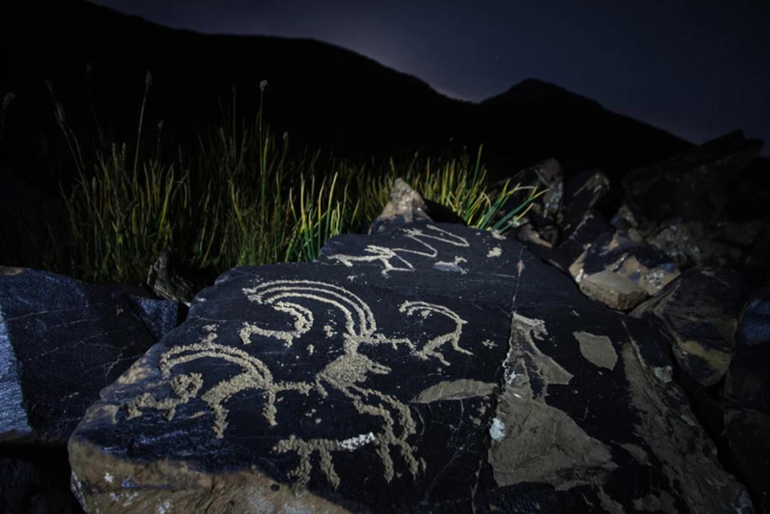 سنگ‌نگاره‌های باستانی (Petroglyphs) حک شده روی صخره‌های تیره در کوهستان