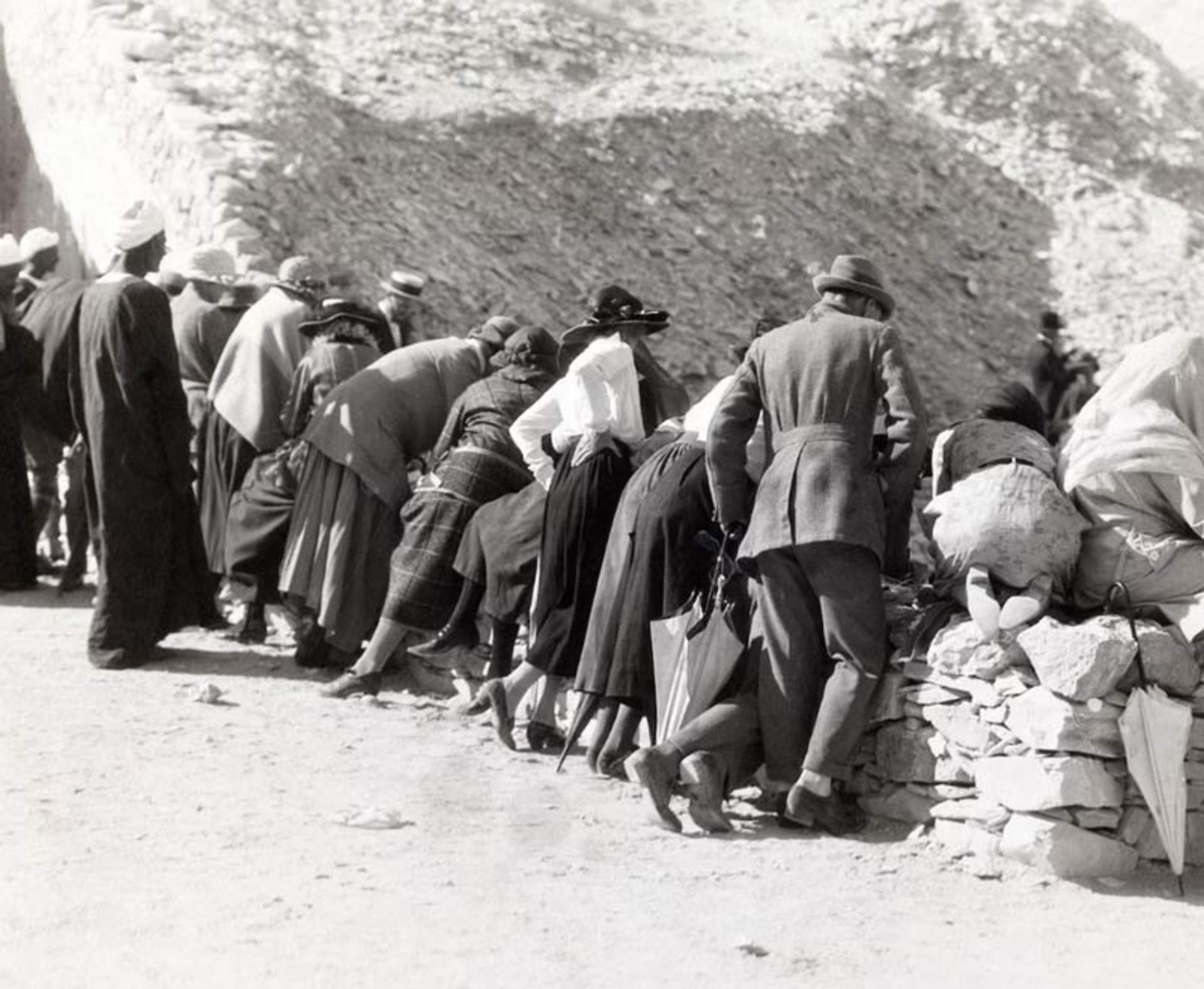  بازدیدکنندگان اروپایی در حال خم شدن روی لبه سنگی برای تماشای داخل مقبره توت‌عنخ‌آمون