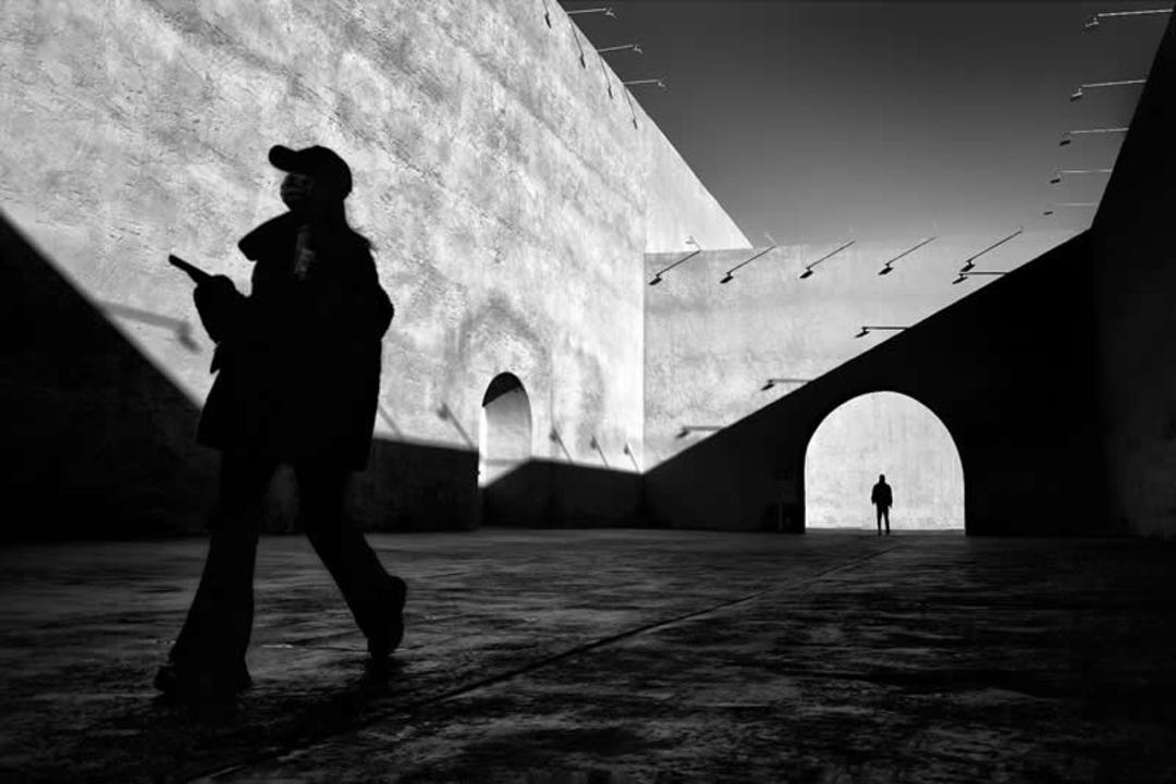 سایه یک فرد در میان دیوارها و قوس‌های معماری با نورپردازی تند