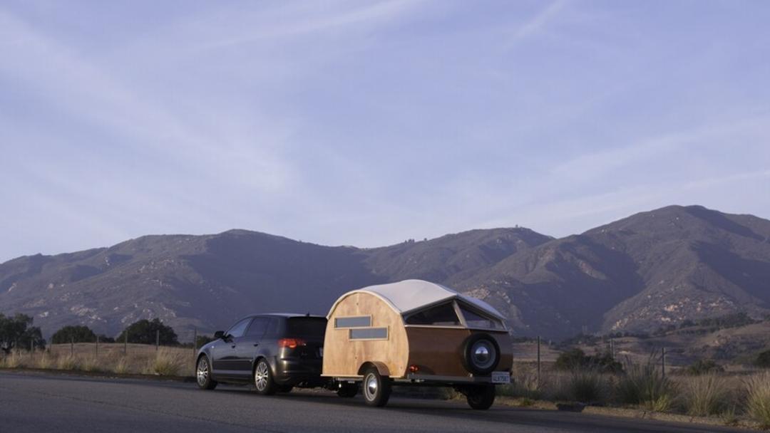 کاروان کوچک (Teardrop Camper) متصل به یک خودرو در جاده‌ای کوهستانی