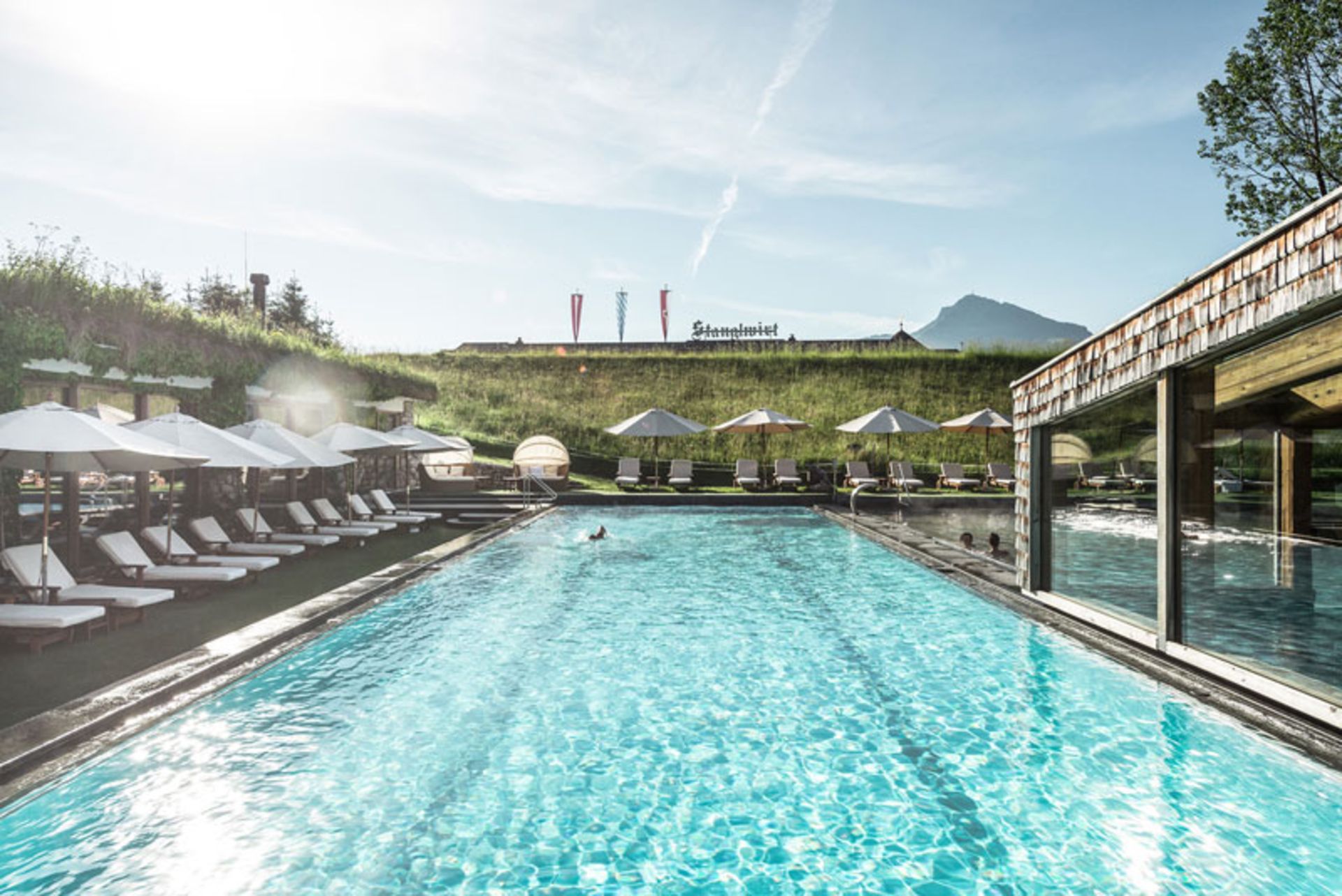 استخر روباز بزرگ هتل اشتانگل‌ویرت با صندلی‌های آفتاب‌گیر و پس‌زمینه‌ای سرسبز