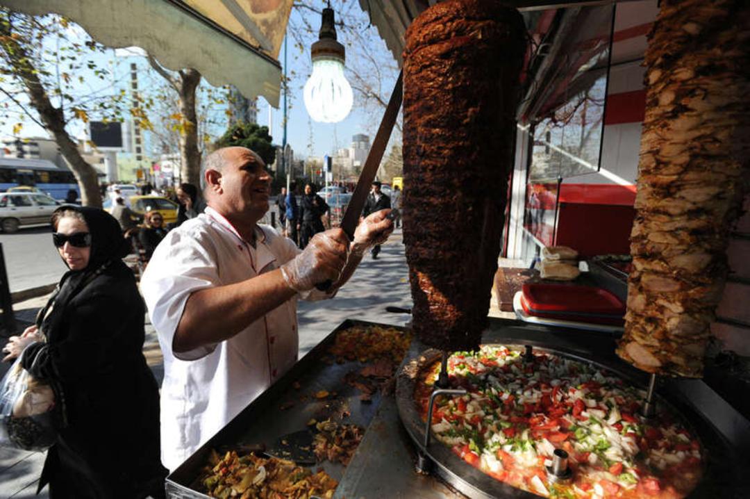 آشپز در حال برش زدن کباب شاورما (Shawarma) در یک مغازه خیابانی