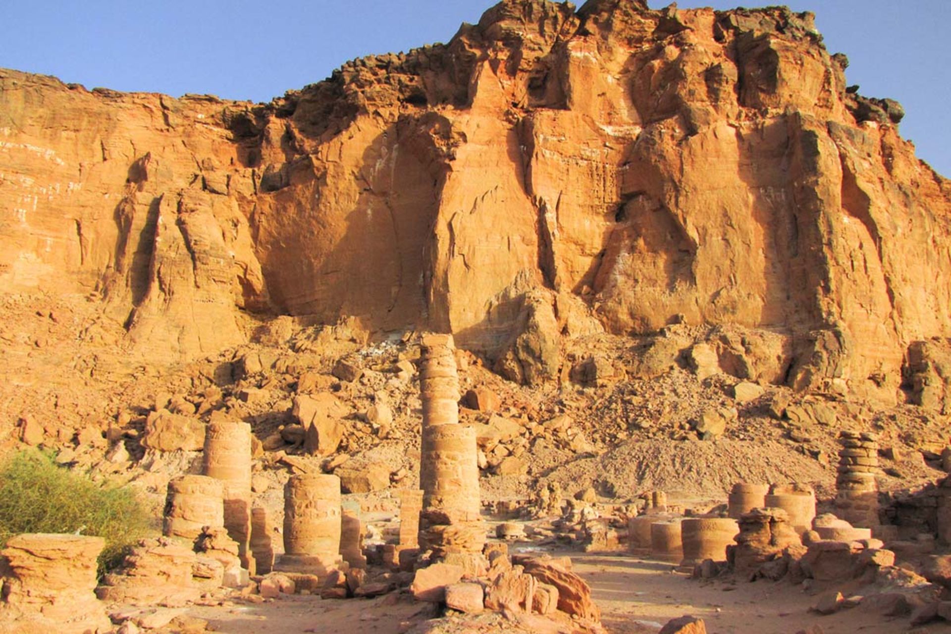 نمای صخره‌های بلند و نارنجی‌رنگ در صحرای سودان به همراه بقایای ستون‌های سنگی کوتاه