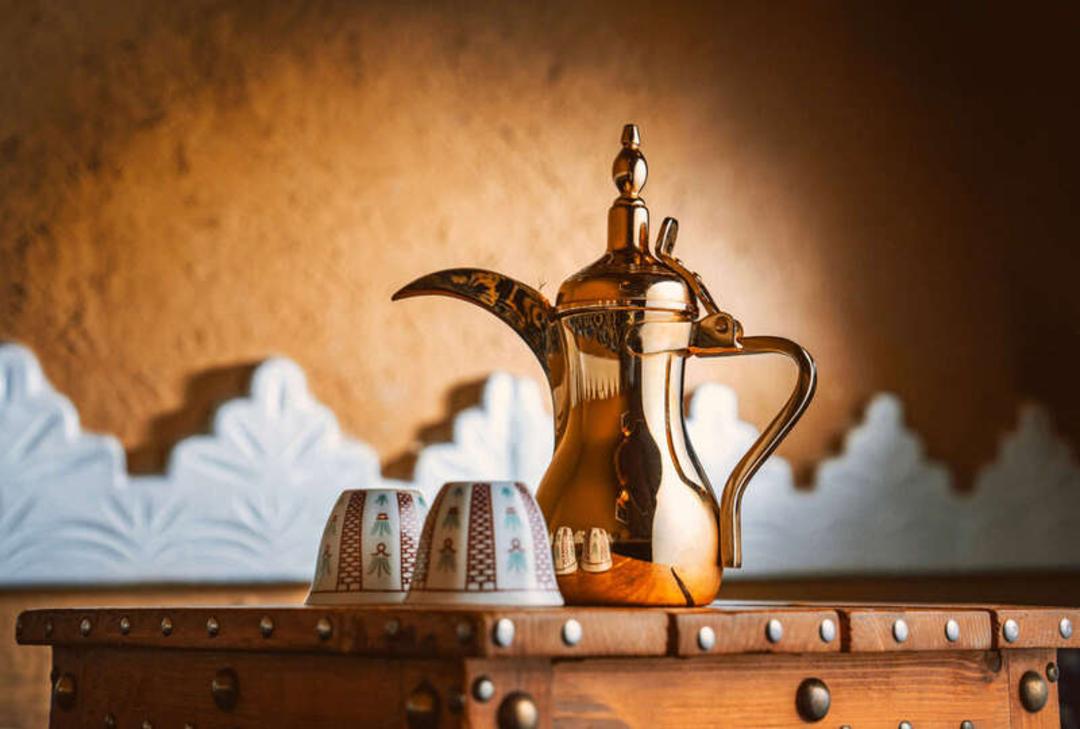 قوری مسی سنتی و فنجان‌های کوچک چای روی یک میز چوبی