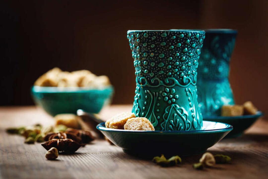 فنجان‌های چای با طرح‌های اسلیمی و ظرف‌های کوچک حاوی شیرینی