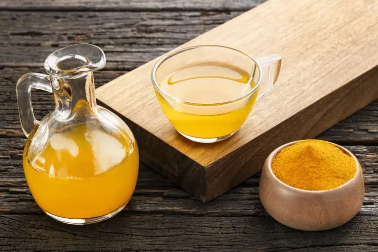 پودر زردچوبه (Turmeric) در کنار نوشیدنی زرد رنگ در فنجان و پارچ شیشه‌ای