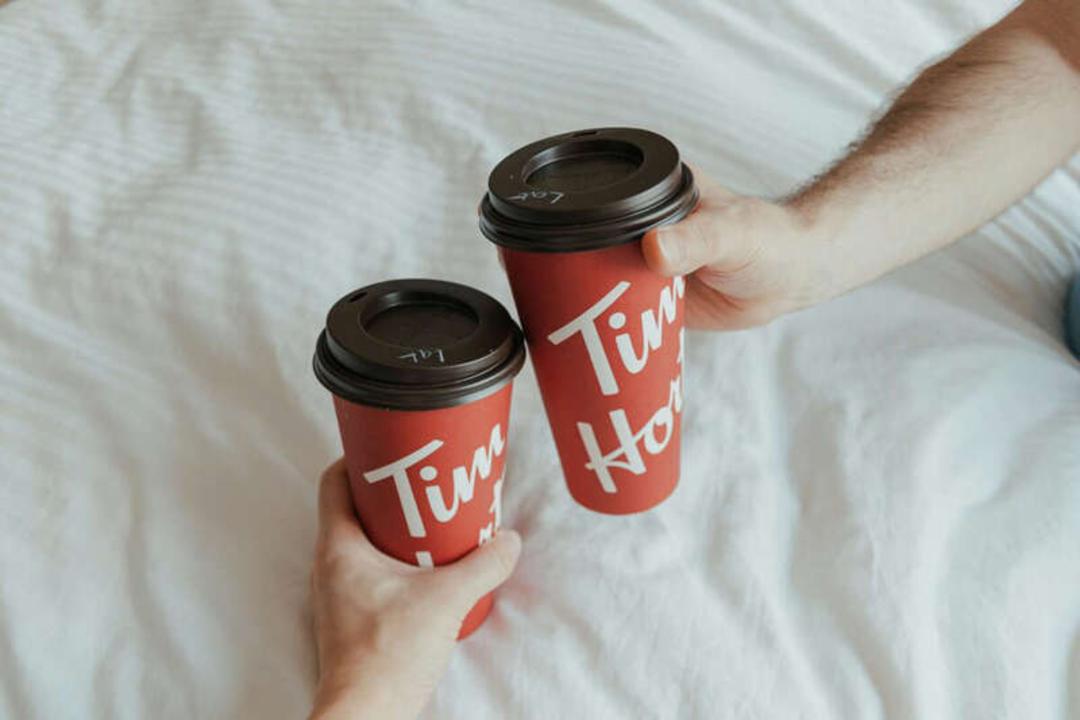 دو فنجان قهوه قرمز رنگ برند تیم هورتونز (Tim Hortons) روی رختخواب سفید