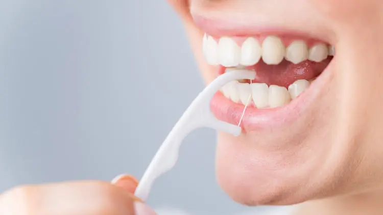 نخ دندان (Dental Floss) در حال تمیز کردن میان دندان‌های یک زن