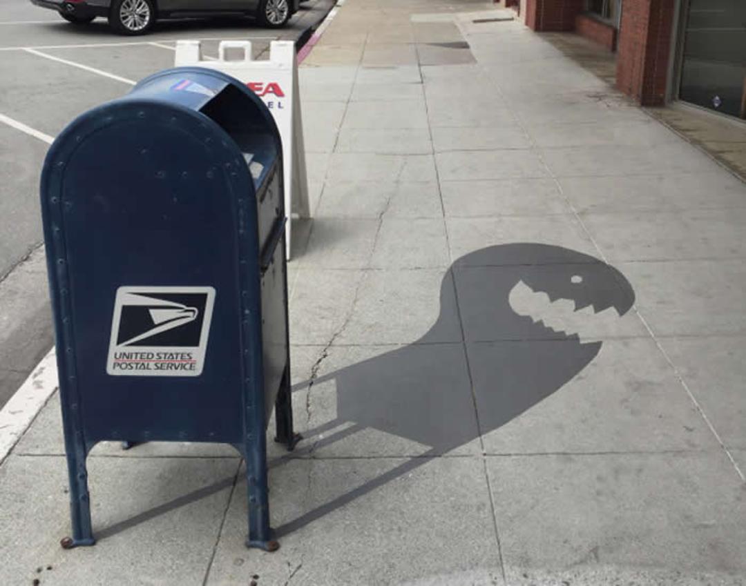سایه صندوق پستی United States Postal Service (USPS) به شکل سر یک دایناسور روی پیاده‌رو