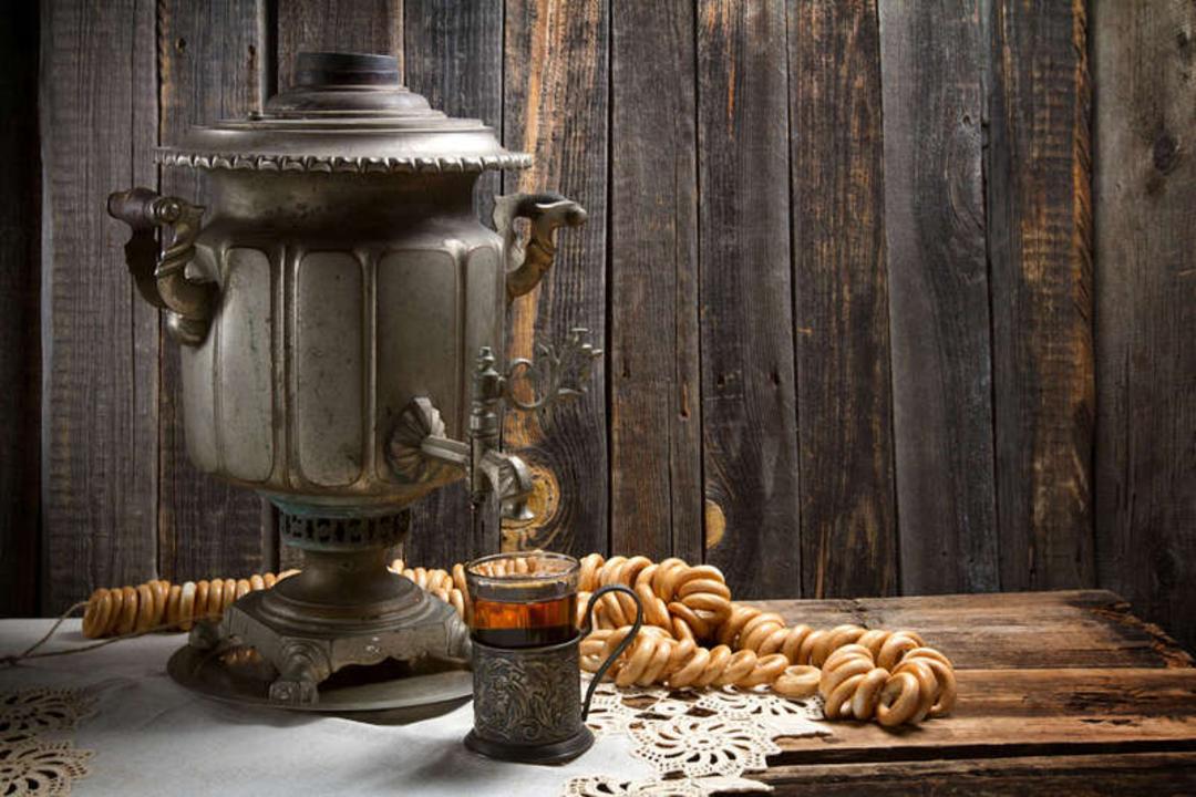 سماور قدیمی (Samovar) فلزی در کنار فنجان چای و حلقه‌های نان سنتی
