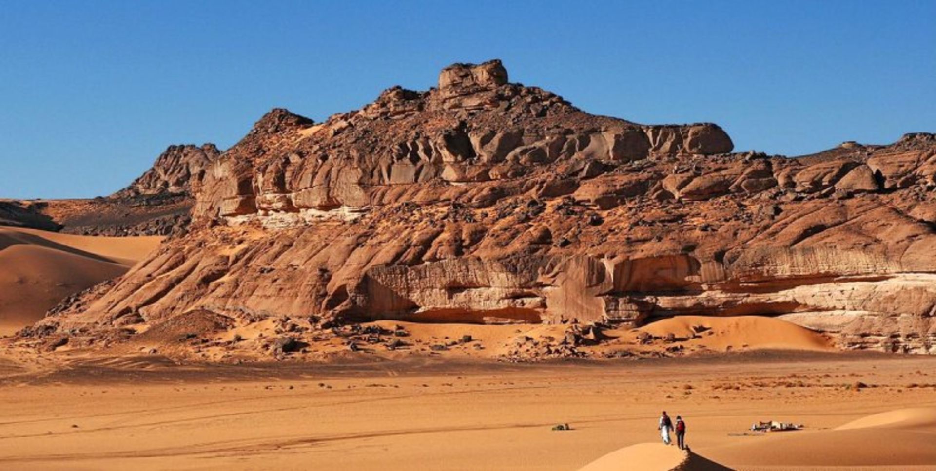 ماسه ها، کوه ها، آسمان صاف و آبی و دو فرد در بیابان عزیزیه