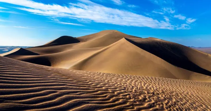 ماسه های صاف و موج دار و آسمان آبی با ابرهای سفید در کویر لوت