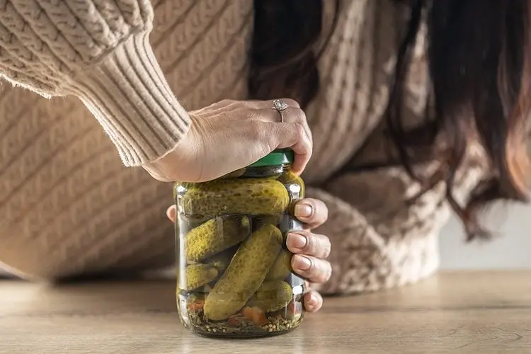 خیارشور داخل یک شیشه شیشه‌ای در دست یک زن